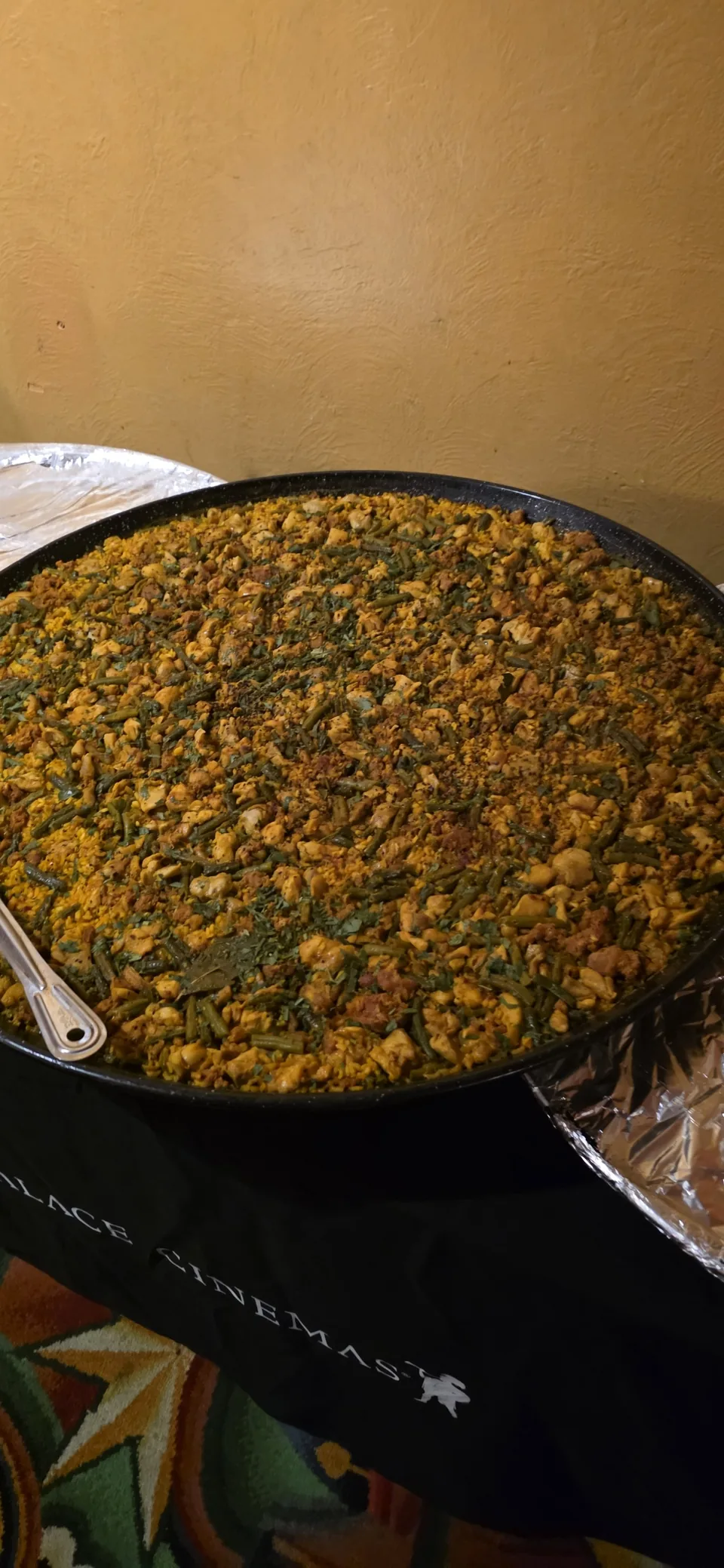 A large pan of chicken paella with green beans and a serving spoon