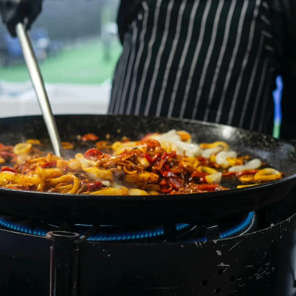 Seafood and peppers cooking in a paella pan over a gas flame