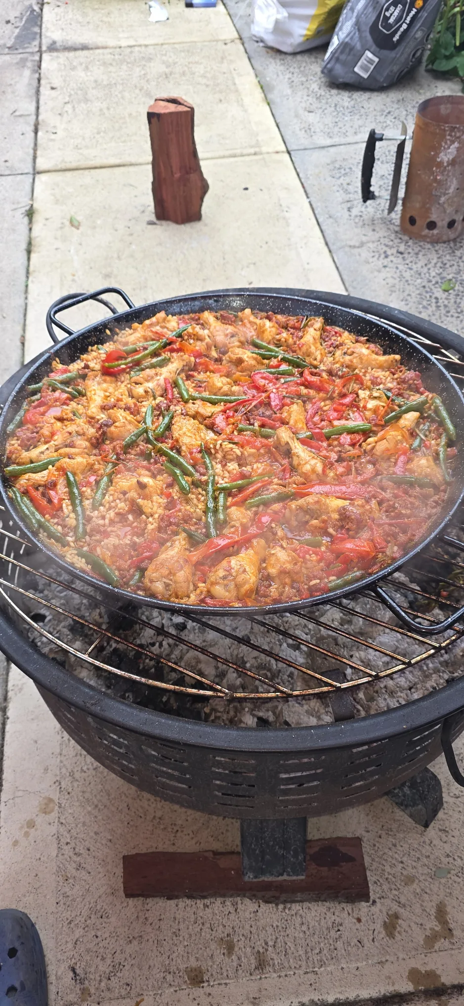 A pan of paella cooking outside, with red peppers and green beans