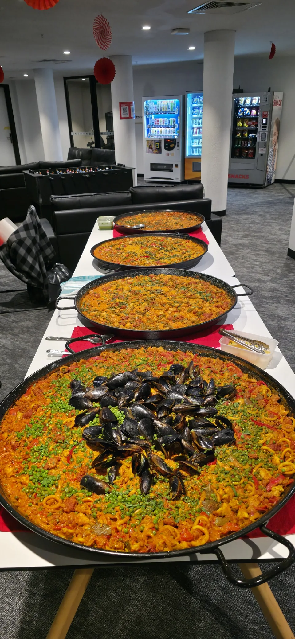 Large pans of paella arranged along a table, with mussels in the nearest pan
